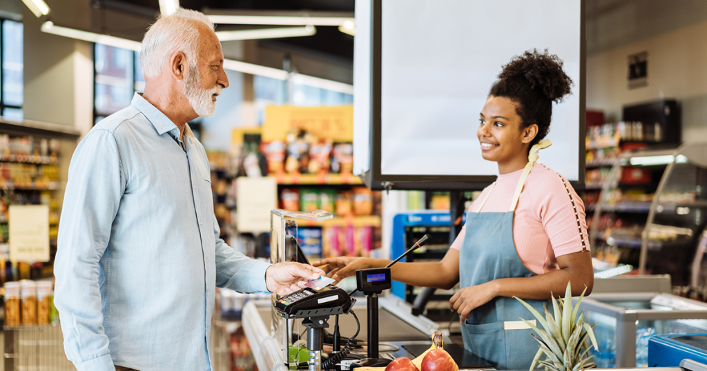 Man shopping at grocery store provides his credit card to clerk.