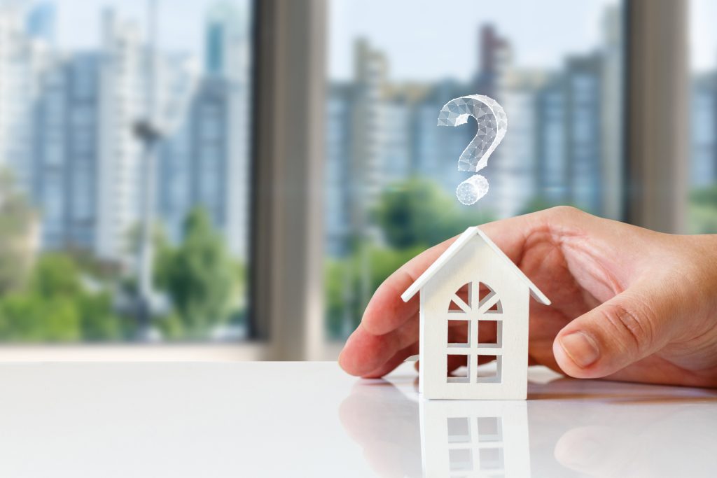 Hand placing down a small home figurine with question mark above it.