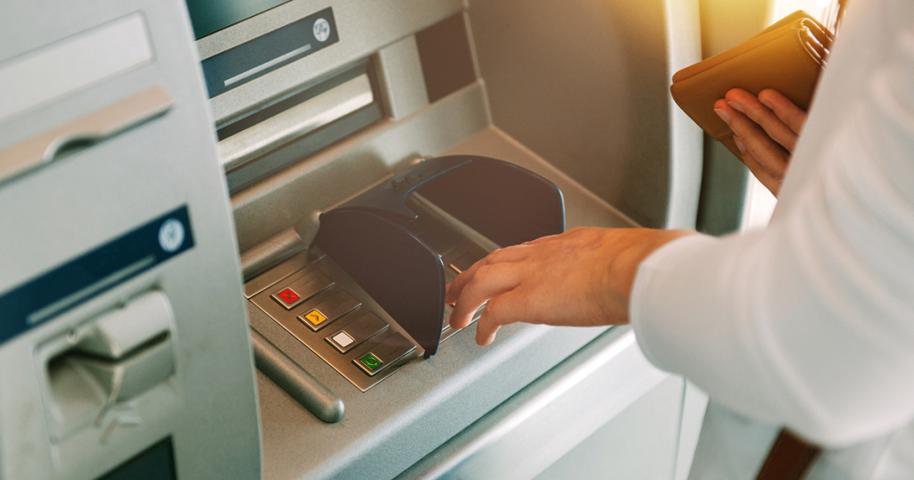 Someone at ATM punching in pin code with wallet pictured.